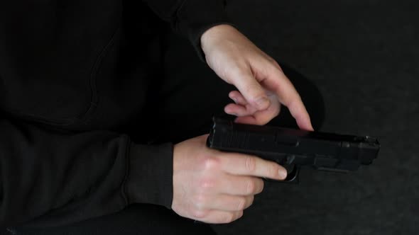 A man loading and cocking a pistol hand gun while sitting down