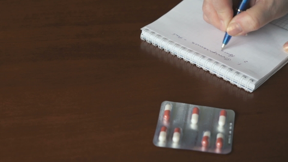 Female Hand Writes a Note About Taking Tablets