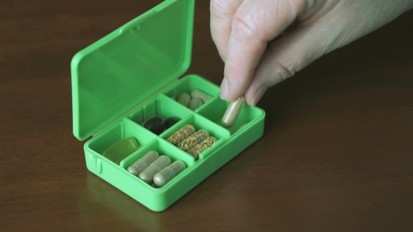 Hand Puts Pills In a Container For Tablets
