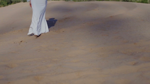 Feet Of Woman Walking On Beach Dunes In White Dress