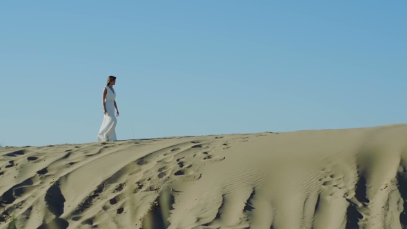 Woman In White Dress Walks On Sand Dune 