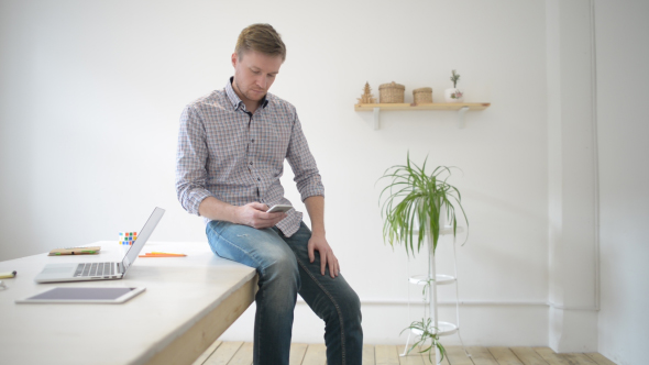 Designer Sitting at Desk, Texting on Smartphone