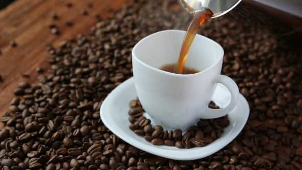 Pouring Coffee In Cup Surrounded By Coffee Beans