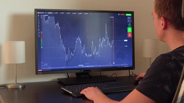 A Man Sits at a Table and Examines a Chart on a Computer Screen