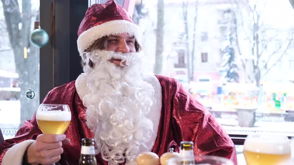 Santa Claus with a Big Gray Beard is Drinking Beer From a Glass He is Relaxing with Friends