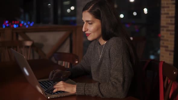 Young Smiling Woman Is Sitting with a Notebook in Restaurant in Evening