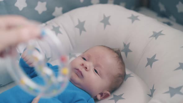 Mother Plays with Small Son Shaking Funny Rattle Above Crib