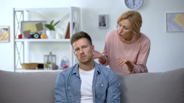 Disappointed Mom Talking to Lazy Adult Son Sitting on Sofa at Home, Upbringing