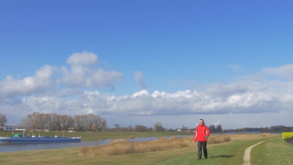 Backpacker is Walking Along a River Toward Camera