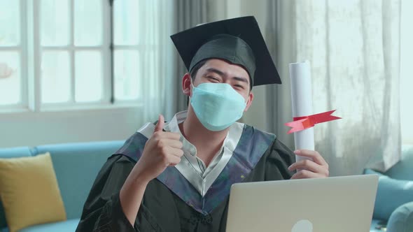 Man Wearing Protection Face Mask, Thumb Up And Showing A University Certificate To Camera At Home