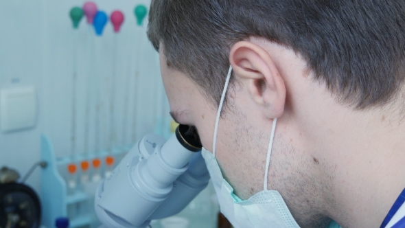 Young Doctor Or Laboratory Researcher Looking Through The Eyepiece Of a Microscope.