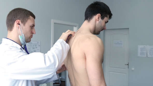 Doctor Examining Back Of Young Male Patient With Stethoscope
