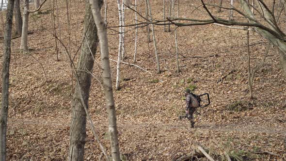 Side view of bowhunter holding hunting equipment walking on winter forest path