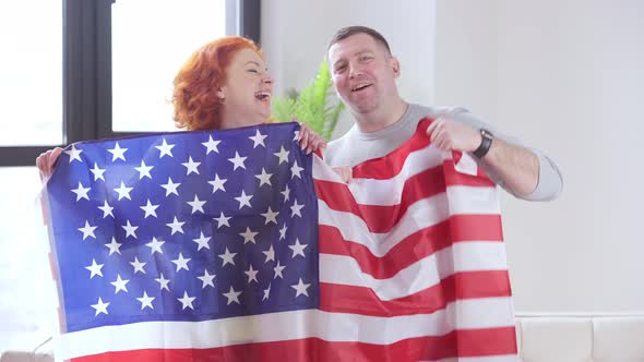 Proud Adult Couple Posing with American Flag Showing Thumb Up and Looking at Camera with Toothy
