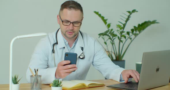 Male Doctor in White Coat Using Modern Smartphone Device with Touch Screen. Doctor Using Mobile