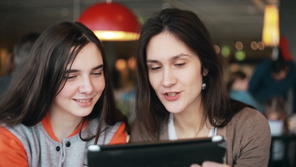 Two Girls Sisters Using Tablet Talking In Cafe