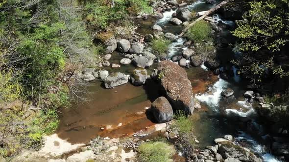 Drone footage moving up river in a valley of trees. Pristine clean water flowing between rocks and b