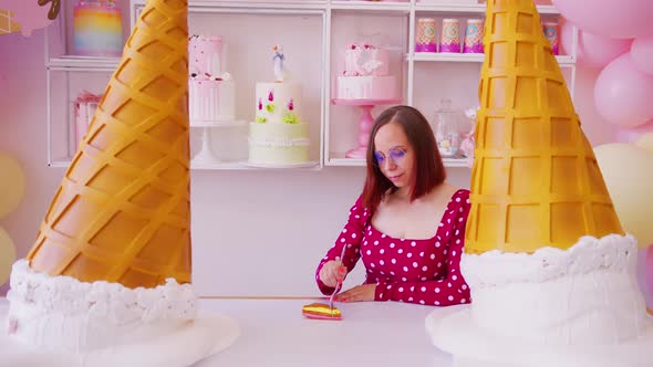 Young woman in glasses eating cake with fork, standing in vivid confectionery.