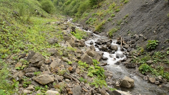 Water Stream In Mountains Flows Between Rocky Hills In Summer