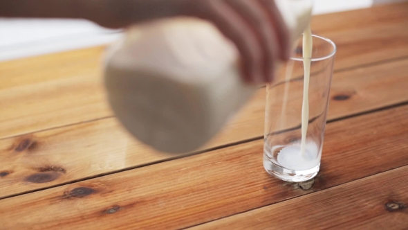 Hand Pouring Milk Into Glass On Wooden Table 11