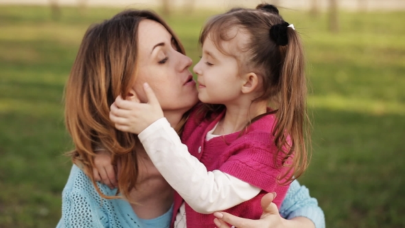Little Girl Kisses And Hugs Her Mother In The Park