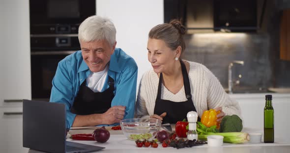 Senior Couple Using Laptop While Cooking in Kitchen at Home