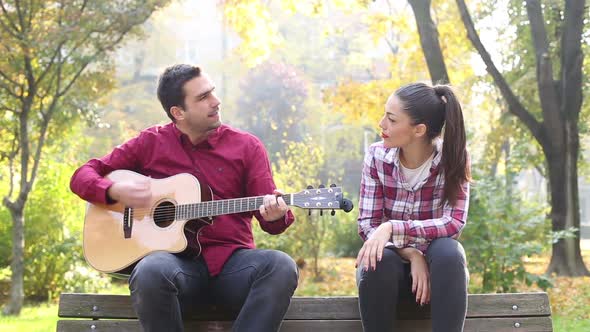 Man Playing Guitar And Singing With Women While Sitting On Bench In Park 2