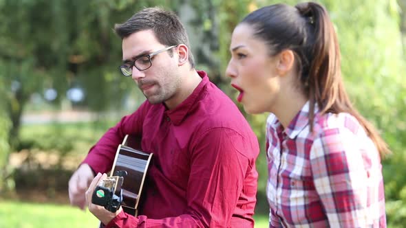 Young Couple Playing Guitar And Singing In Park 1