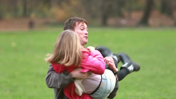 Young Dad Holding Daughter In His Arms And Laughing In Park
