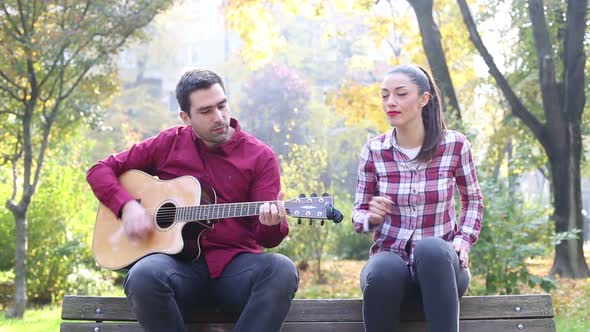 Young Man And Women Playing Guitar And Singing In Park 1