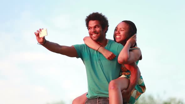Young Man Giving His Girlfriend A Piggyback Ride While Taking Selfie