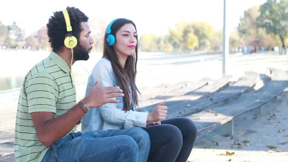 Couple Having Fun Listening To Music On Headphones At The Park 2