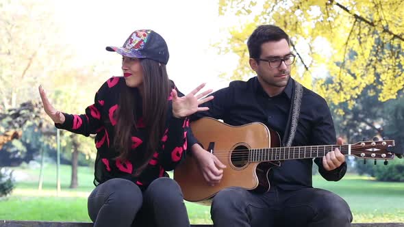 Couple Having Fun Sitting On Park Bench And Playing Guitar