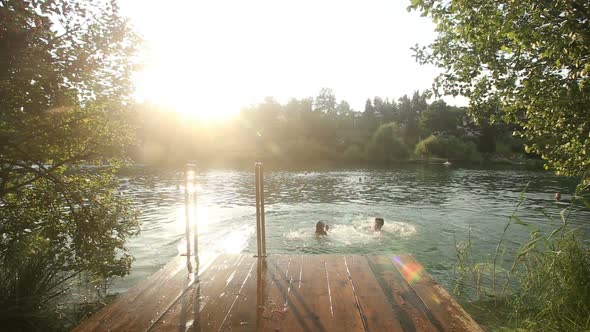 Couple Holding Hands And Jumping Into Water From River Dock