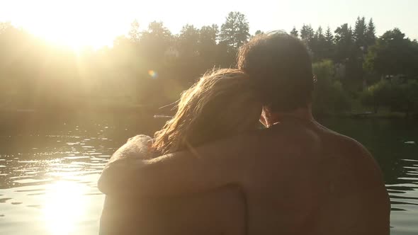 Back View Of Couple In Love Sitting By The River At Sunset