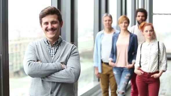 Portrait Of Male Advertising Executive Smiling, Colleagues In Background