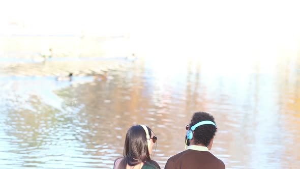 Couple In Love Sitting By Lake And Listening To Music With Headphones