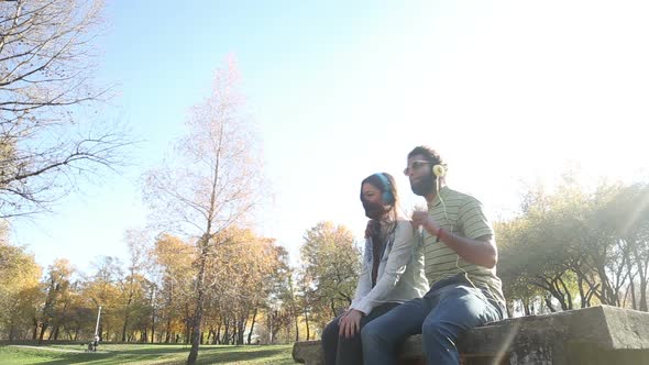 Couple Listening To Music On Headphones While Hanging Out In Park 3