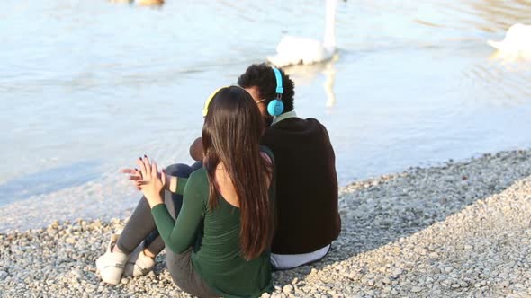 Couple Listening To Music With Headphones, Sitting By Lake 1