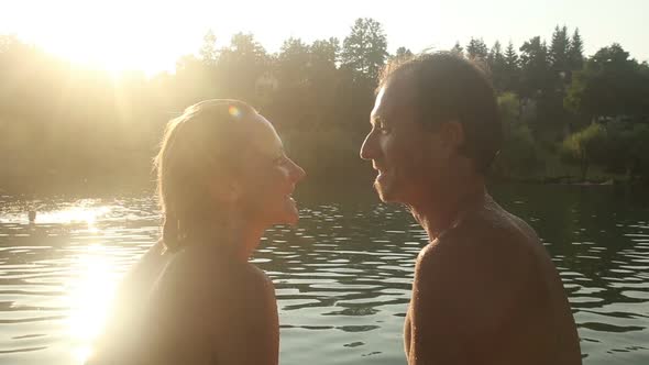 Romantic Couple Looking At Each Other While Sitting By The River At Sunset