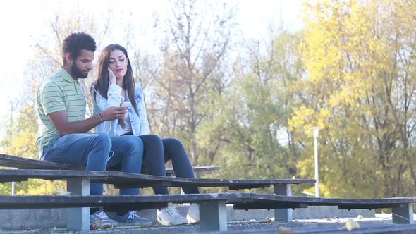 Couple Sharing Earphones While Listening To Music At Park