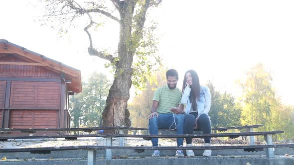 Couple Sharing Earphones While Listening To Music On Smartphone 1