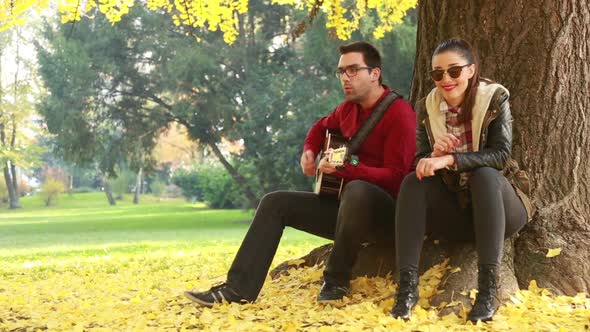 Couple Singing And Playing Guitar While Sitting On A Tree