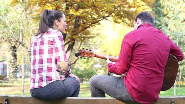 Couple Sitting On Park Bench, Man Playing Guitar While Woman Singing 4