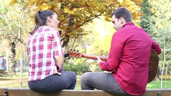 Couple Sitting On Park Bench, Man Playing Guitar While Woman Singing 5