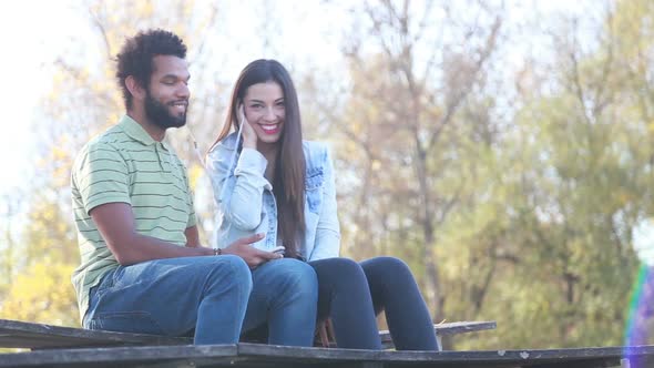 Cute Couple Sitting On Bench And Listening To Music On Shared Earphones 2