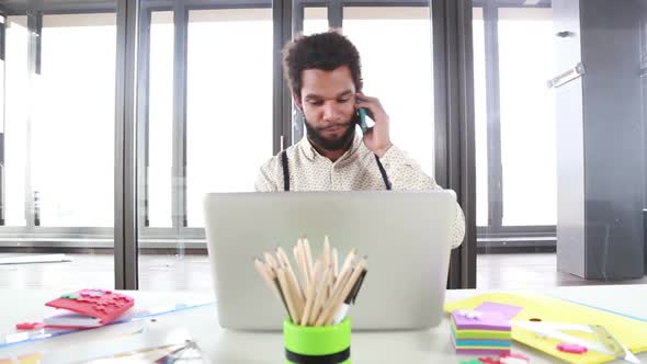 Male Creative Executive Talking On Phone While Working On Laptop