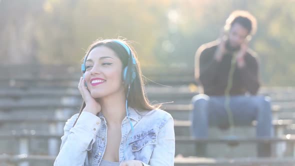 Woman Listening To Music On Headphones, Man Blurred In Background