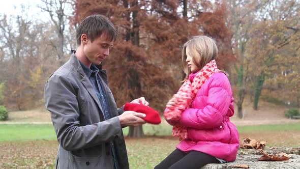 Dad Putting Red Cap On Daughter's Head And Scarf In The Park