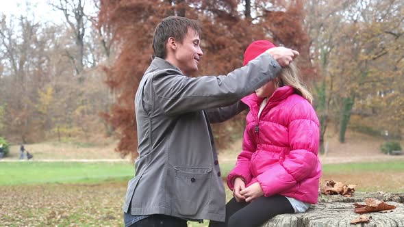 Father Helping Daughter Put On Jacket And Putting Her Cap On The Head